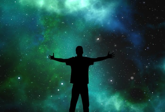 A silhouette of someone with arms held out looking up to space