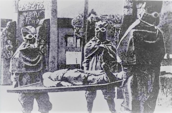 A picture of three men in bio-suits carrying someone on a stretcher