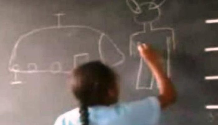 One of the children draws an example of the alien figures on the blackboard 