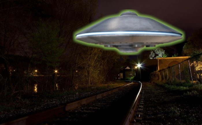 A depiction of a UFO hovering over a rail track