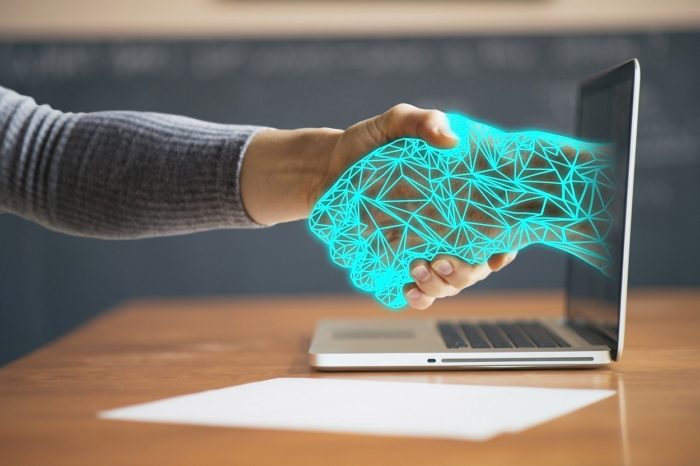 A human hand shaking hands with an artificial hand reaching out of a screen