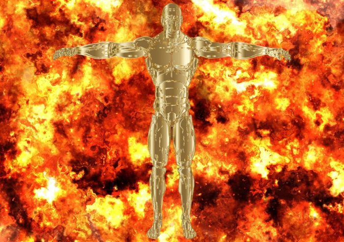 A gold robotic figure standing with a backdrop of flames