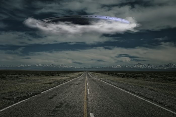 An image of a UFO emerging from cloud over a lonely road