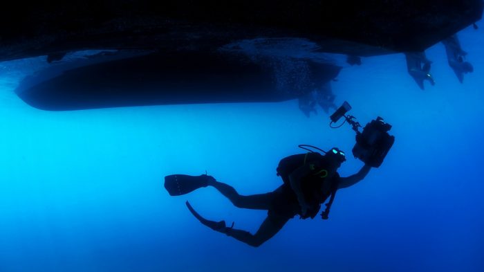 An underwater diver under the water underneath a boat