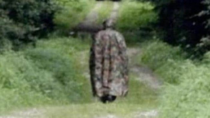 A picture of a cloaked man walking away from the camera on a country path 