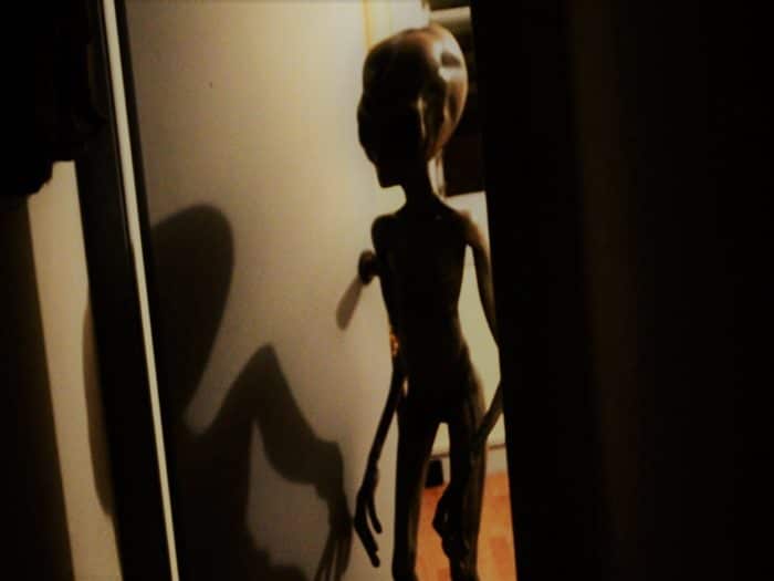 A depiction of a grey alien entering a room