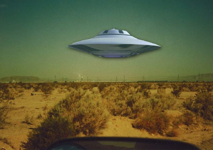 A depiction of a UFO hovering over a desert 