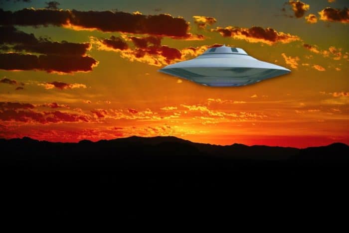 A silver UFO in a sunset sky