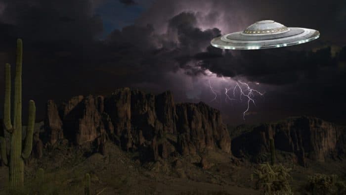 A depiction of a UFO over a desert landscape at night