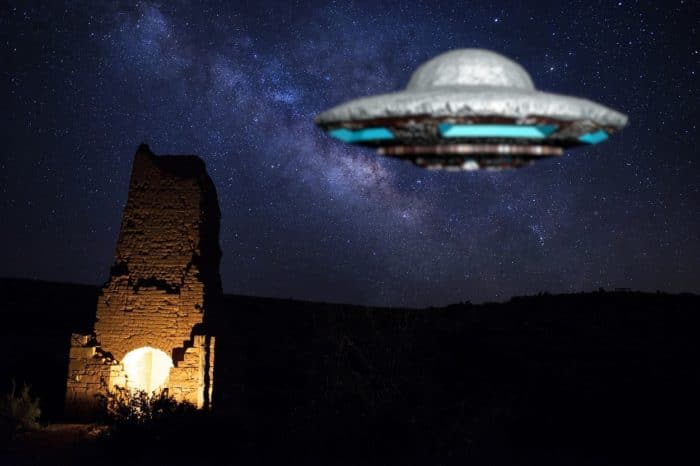 A depiction of a UFO hovering over a ruined building at night