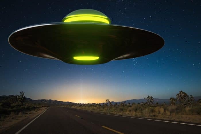 A depiction of a UFO hovering over a lonely road