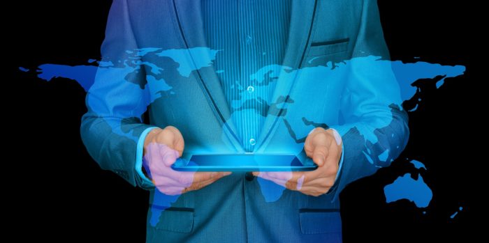 The torso of a suited person holding a tablet with a projection of the world coming from it