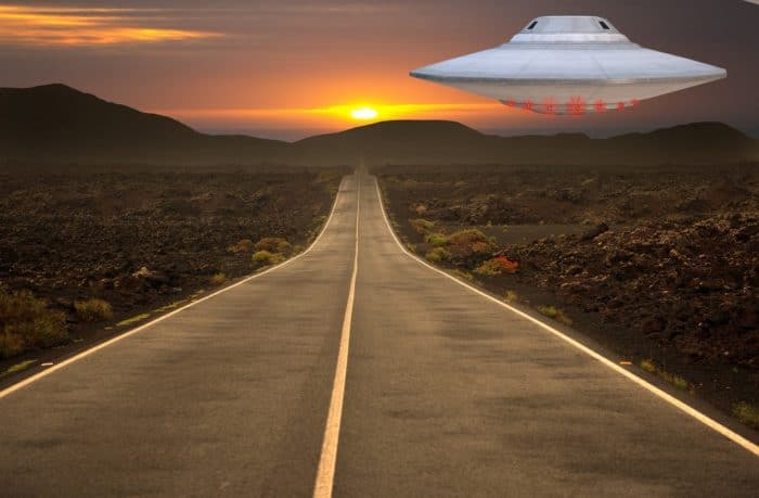 A superimposed UFO over a lonely highway at sunset