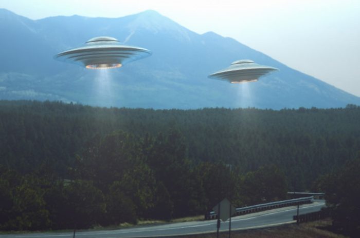 A depiction of UFOs hovering over a highway with surrounding forests