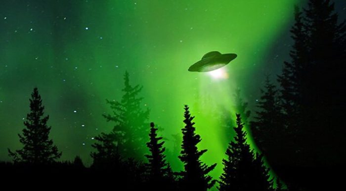 An image of a UFO in a green glowing sky above woodland