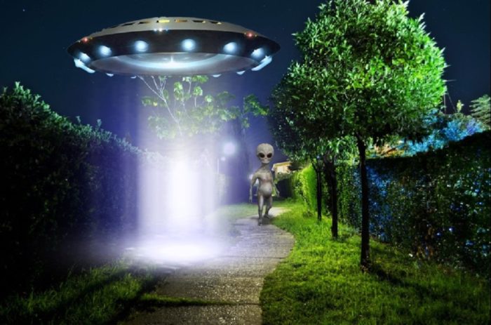 An image of a low-hovering UFO with a grey alien walking from it