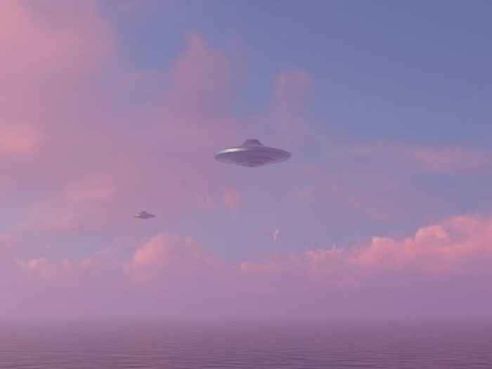 An image showing two UFOs hovering in the sky at sunset