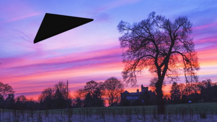 a superimposed black triangular UFO on a picture of the countryside at sunset