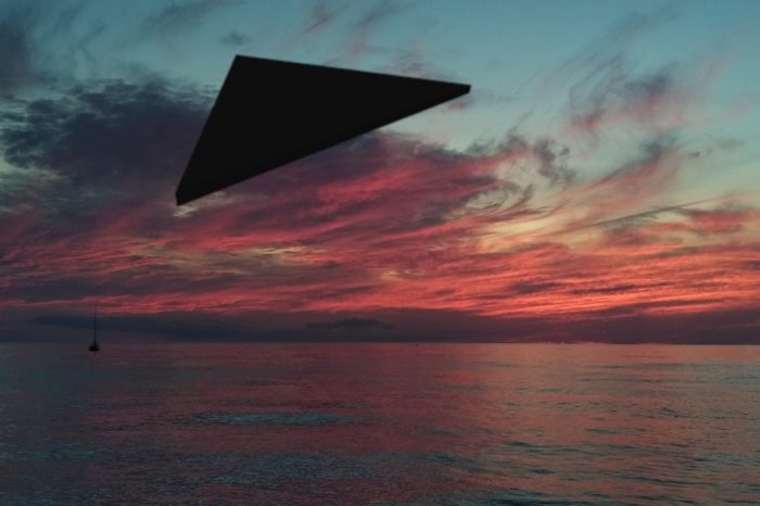 A superimposed black triangular UFO over water at sunset