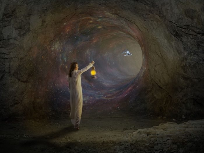 A picture of a person with a lantern staring into a portal in a cave