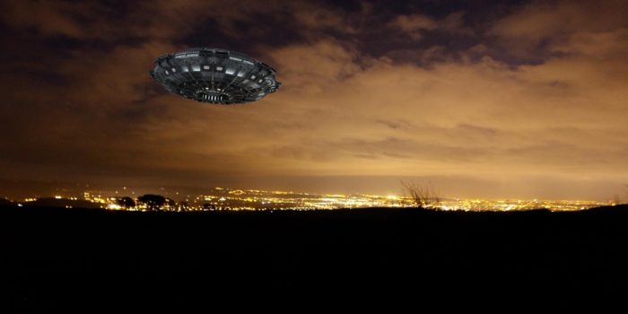 A UFO superimposed onto a night sky with the city lights in the background