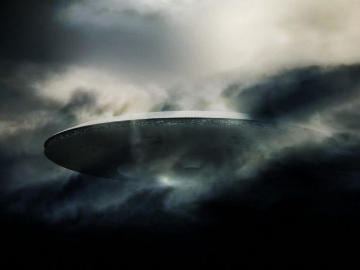 An image showing a huge mothership type UFO emerging from the clouds