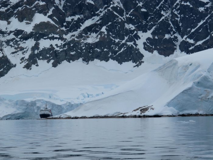 A ship looks tiny compared to icy landmass behind it