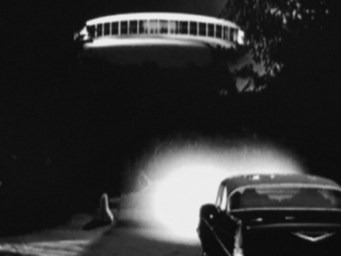 A depiction of a UFO over a parked car