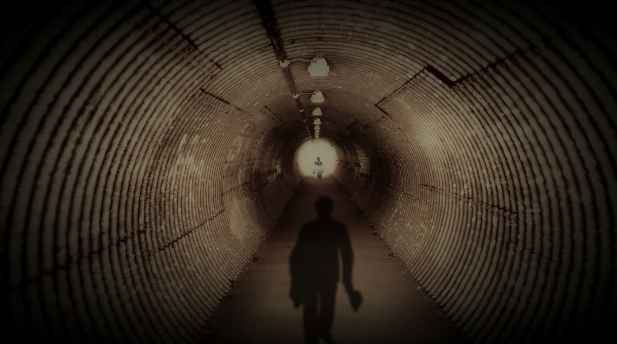 A tunnel with a dark figure walking along it